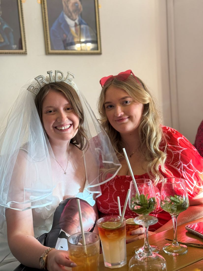 A bride in a veil and her friend smiling with their cocktails
