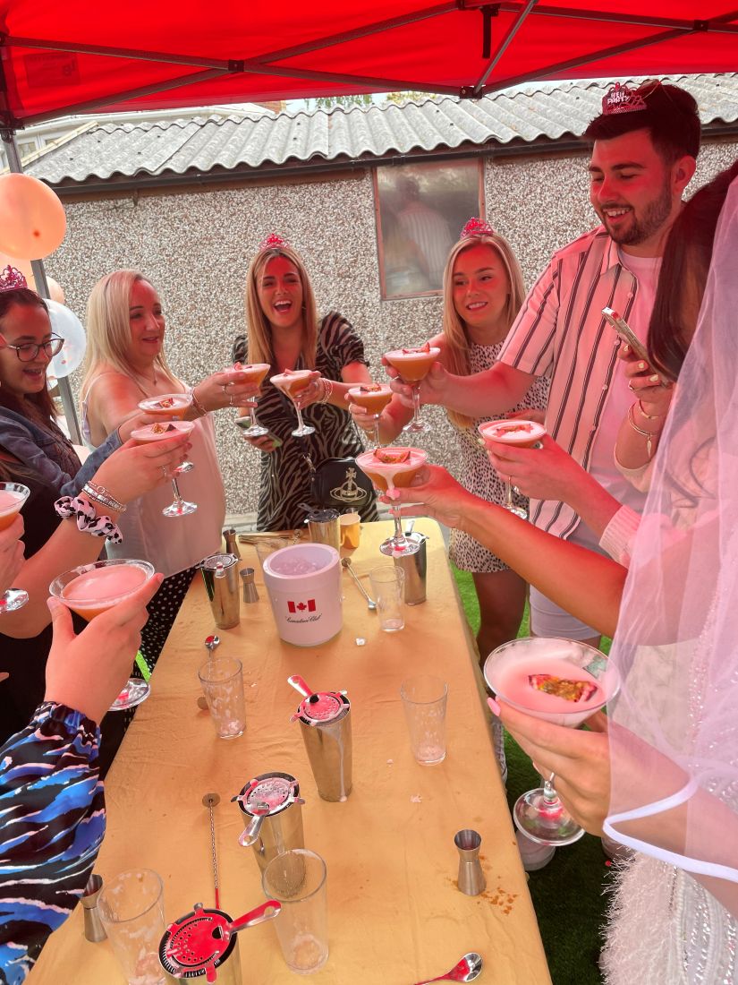 A hen party toasting their cocktails in a garden under a parasol