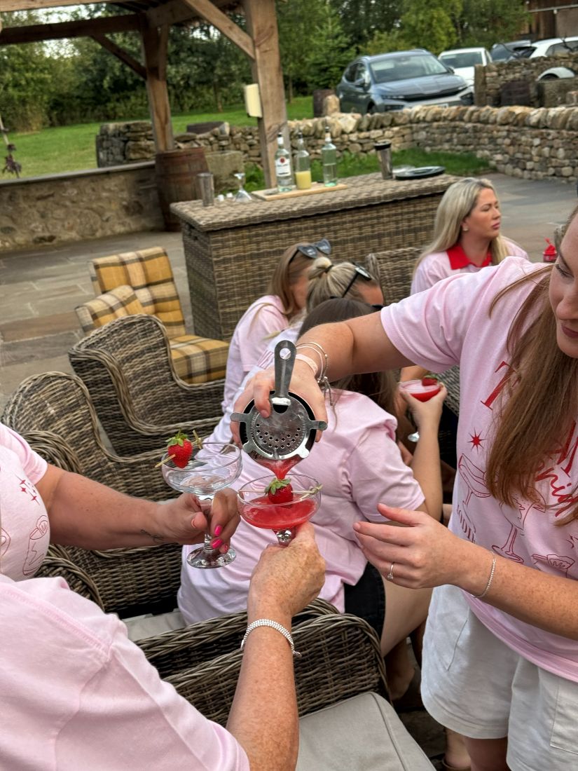 A hen party in matching pink shirts being served freshly strained cocktails in the garden