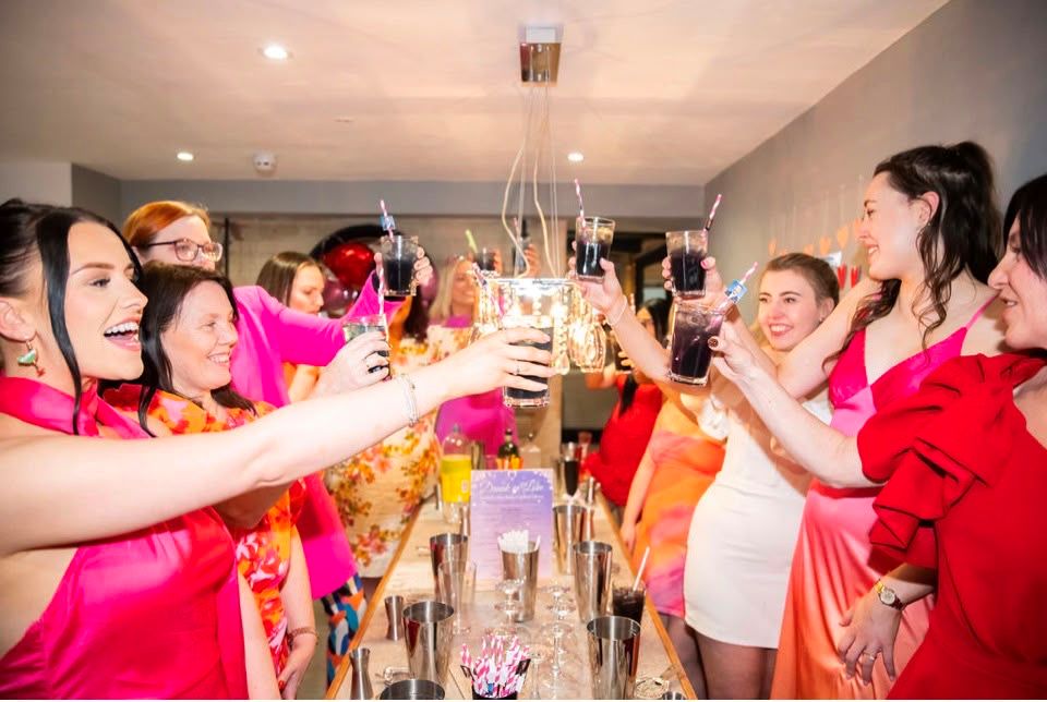 A hen party reaching in to clink their cocktails together across the table