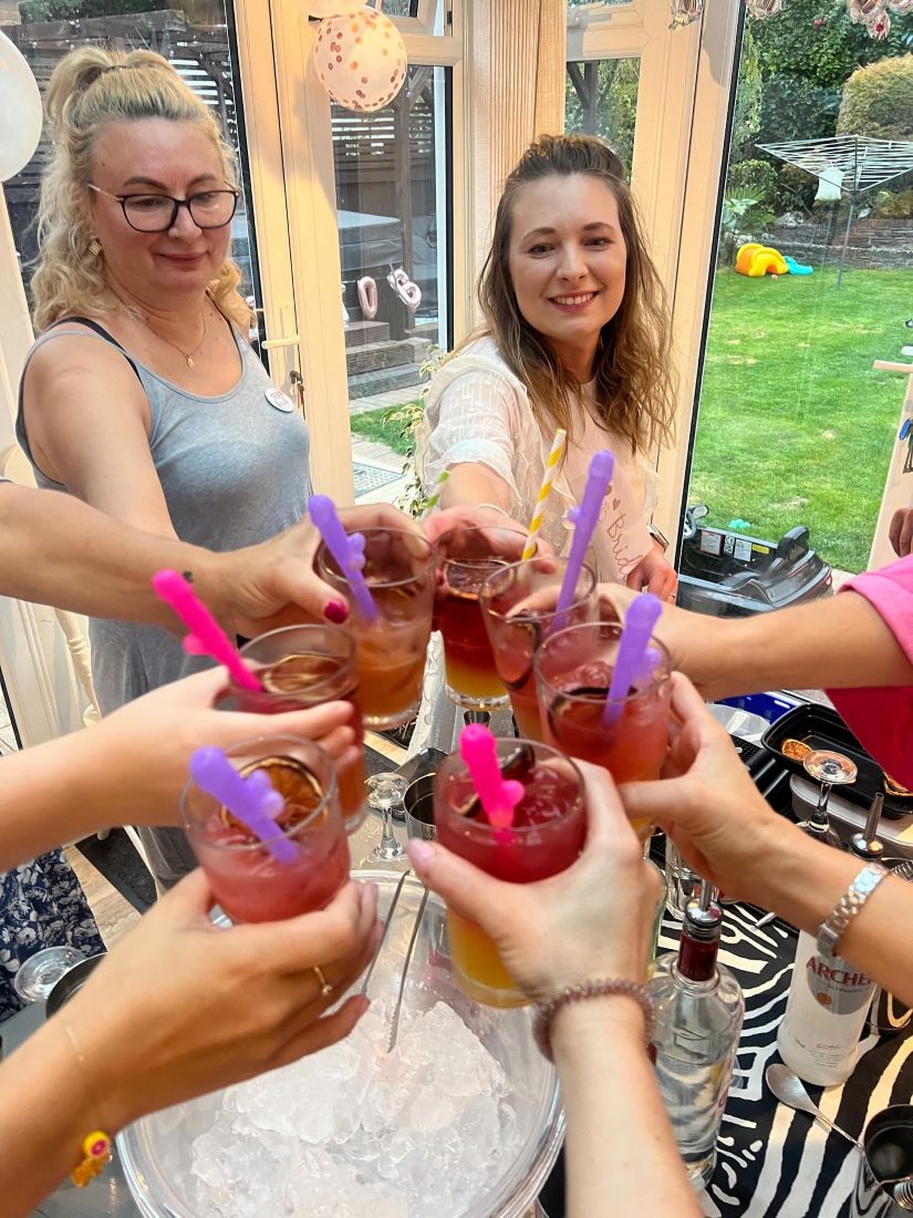 A close-up of six hands clinking tall fruity cocktails over an ice bucket