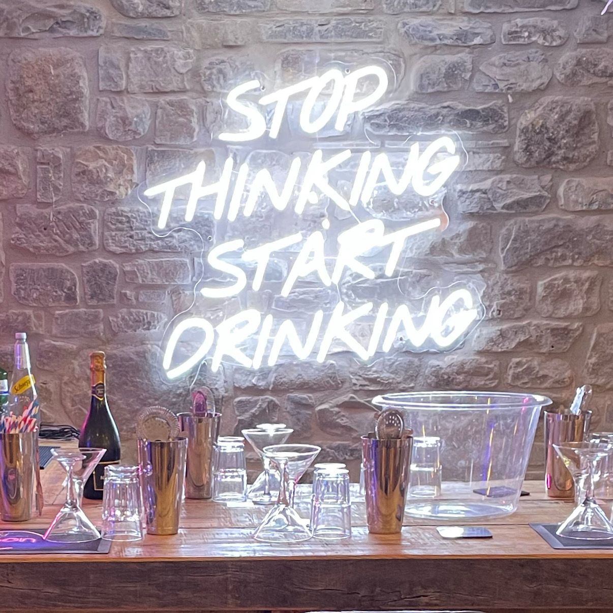 A cocktail bar set up at a venue under a neon sign reading stop thinking start drinking