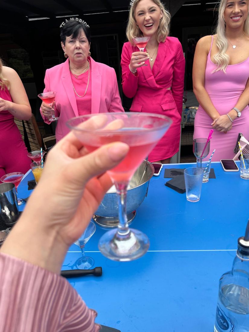 Guests in pink outfits laughing together, a cosmopolitan raised in the foreground