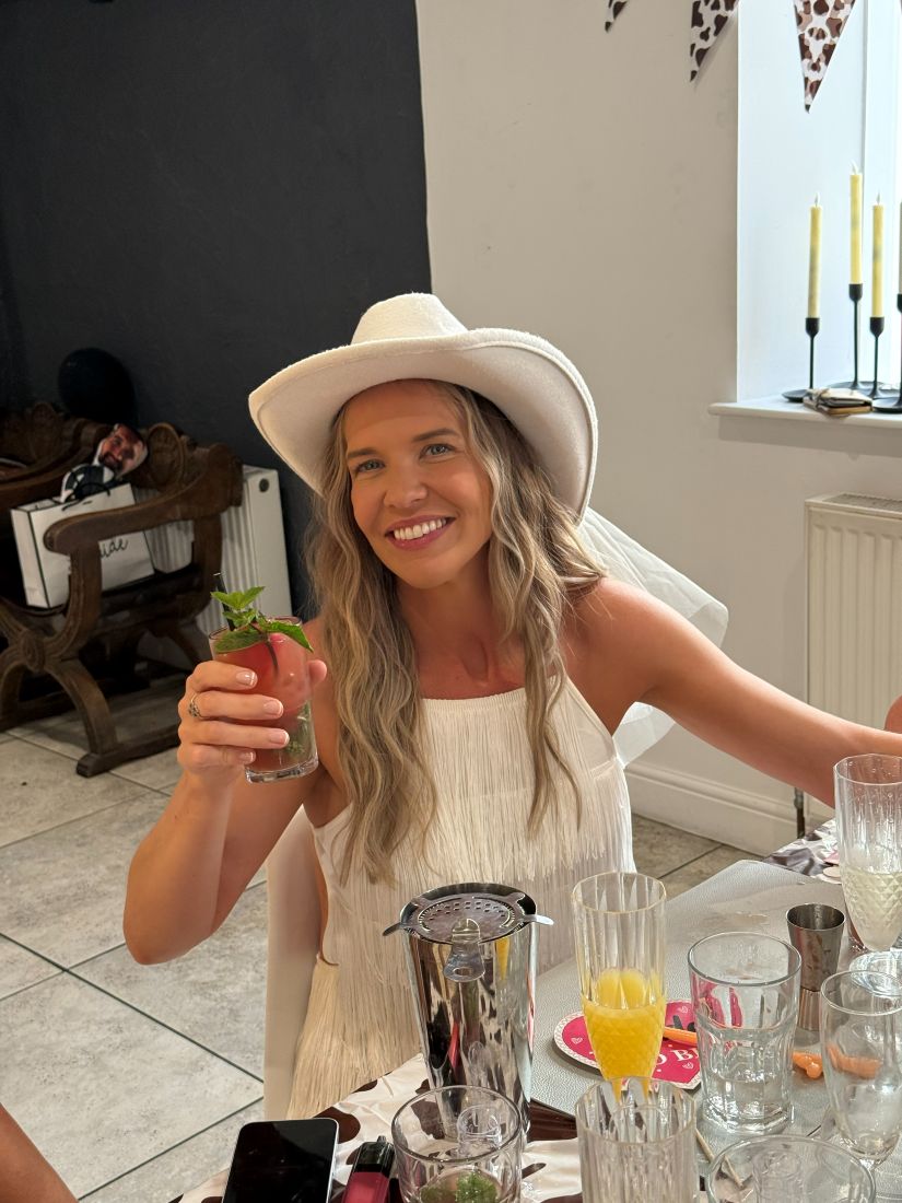A guest in a white cowboy hat grinning as she holds up her mojito